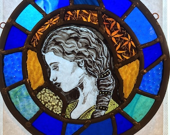 May include: A stained glass window depicting a woman's profile in white and black, surrounded by a blue and yellow border with a floral pattern.