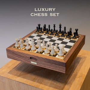 Op de afbeelding: Een luxe schaakset met zwarte en witte stukken op een schaakbord met ruitjes. De set zit in een houten kist met gouden accenten en de tekst "LUXURY CHESS SET". De schaakstukken zijn zwart en wit.