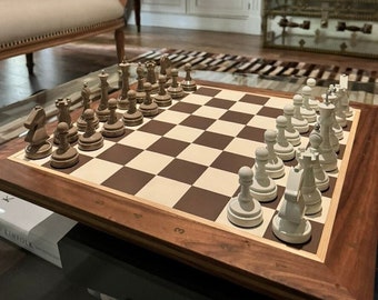 May include: A wooden chess set with light and dark pieces arranged on a brown and beige checkered board. The board is set on a dark wood table. The chess pieces are in the starting positions, ready for a game.