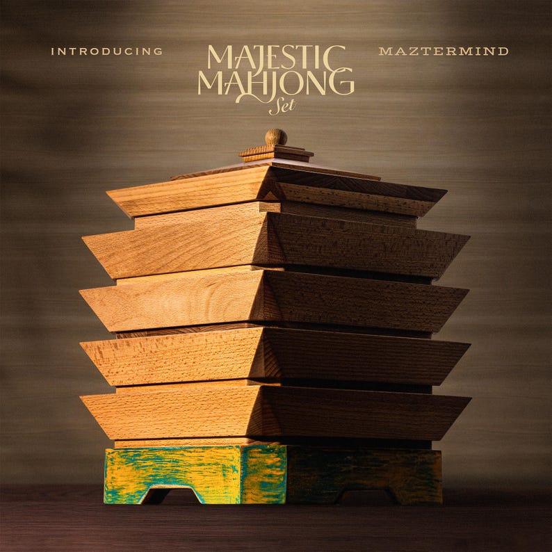 May include: A wooden Majestic Mahjong Set with a tiered design. The set features a stack of light brown wooden boxes, with a base painted in yellow and teal. The text "INTRODUCING MAJESTIC MAHJONG Set MAZTERMIND" is displayed at the top.