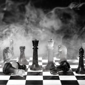 May include: A black and white chessboard with chess pieces arranged in a strategic formation. The board is covered in a thick layer of smoke, creating a dramatic and mysterious atmosphere.