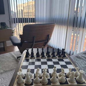 Op de afbeelding: Een schaakspel met zwarte en witte stukken op een schaakbord. Het bord is omlijst met donker hout en een goudkleurige rand. De stukken staan in hun startposities, klaar voor een spel.