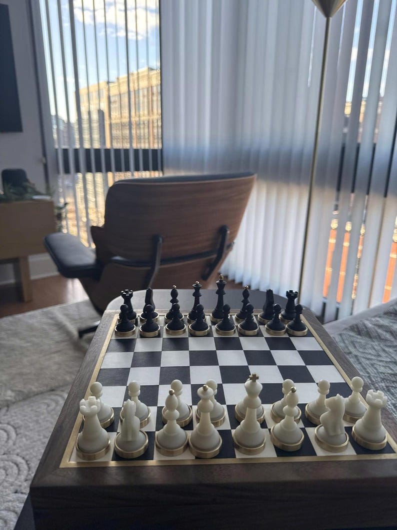 Op de afbeelding: Een schaakspel met zwarte en witte stukken op een schaakbord. Het bord is omlijst met donker hout en een goudkleurige rand. De stukken staan in hun startposities, klaar voor een spel.