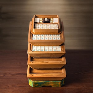 May include: A wooden mahjong set with multiple trays stacked on top of each other. The trays are filled with tiles in various colors and designs. The base of the set is painted green and yellow. The set is made of wood and has a natural finish.