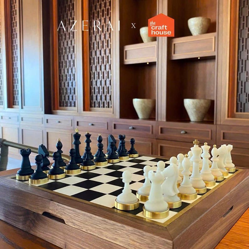 Op de afbeelding: Een houten schaakspel met zwarte en witte stukken op een schaakbord. De zwarte stukken hebben gouden accenten en de witte stukken hebben gouden bases. Het bord staat in een houten kist.