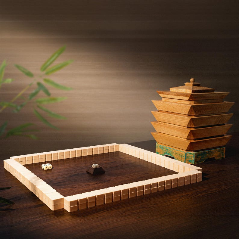 May include: A wooden game set featuring a square playing field with dice and a small pyramid-shaped piece. A stack of wooden boxes resembling a pagoda sits on a teal-painted base. The set is displayed on a dark wooden surface.