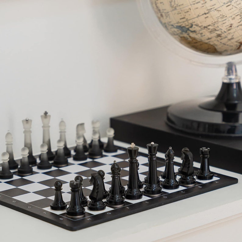 May include: A black and white chessboard with black chess pieces set up on the board. The chessboard is on a white surface with a globe in the background.
