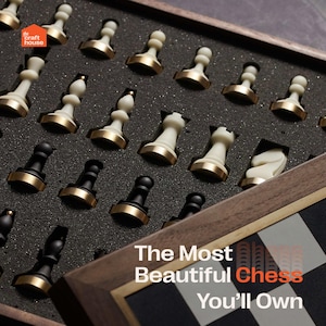 Op de afbeelding: Een houten schaakset met zwarte en witte stukken, sommige met goudkleurige bases, gerangschikt in een met schuim gevoerde doos. De tekst "The Most Beautiful Chess You'll Own" is zichtbaar.
