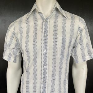 May include: Short-sleeved button-down shirt with a vertical striped pattern in white and blue. The shirt has a classic collar, a single chest pocket, and is displayed on a mannequin. The fabric appears to be lightweight.