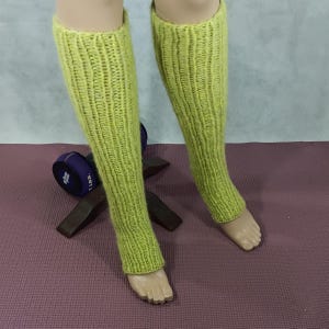 May include: A pair of lime green knitted leg warmers. The leg warmers are made of a soft, fuzzy yarn and have a ribbed texture.