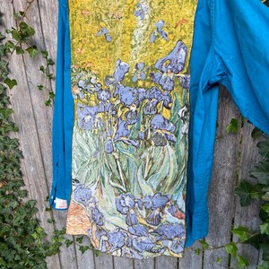 Puede incluir: Una camisa de botones azul turquesa con una pintura de iris p&uacute;rpuras en la espalda. La pintura est&aacute; en un estilo que recuerda a Vincent van Gogh.