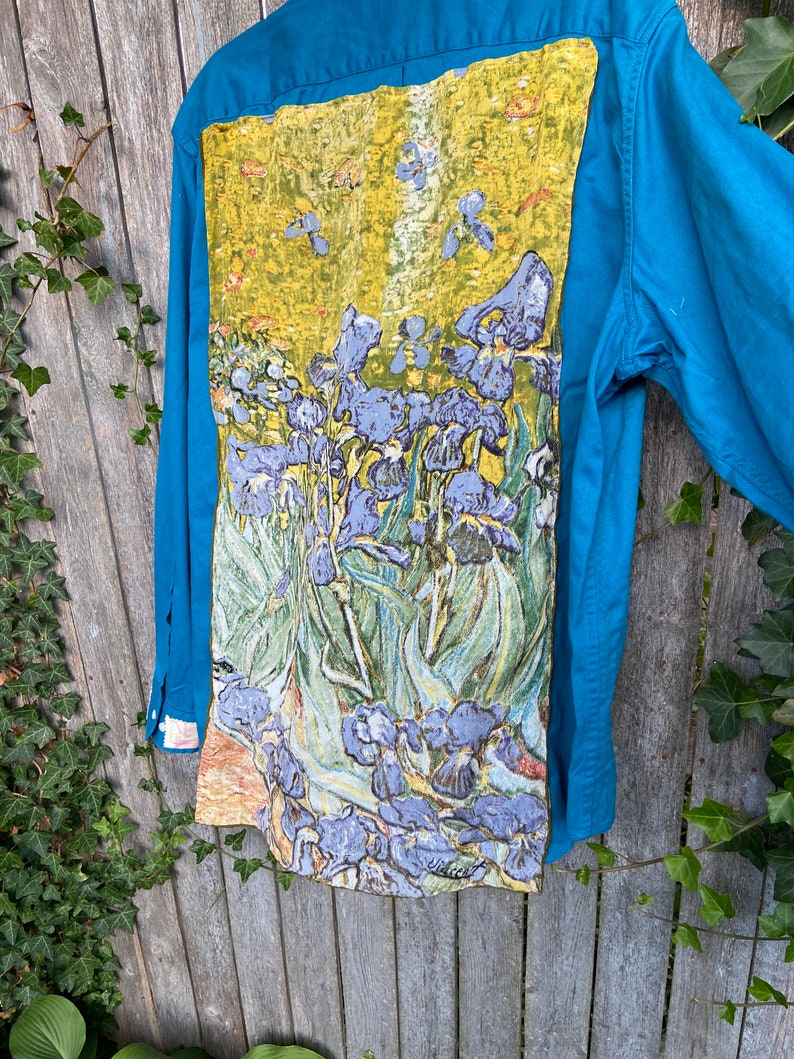 Puede incluir: Una camisa de botones azul turquesa con una pintura de iris p&uacute;rpuras en la espalda. La pintura est&aacute; en un estilo que recuerda a Vincent van Gogh.