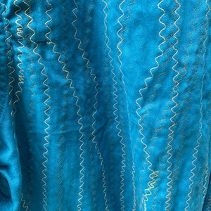 Puede incluir: Tela azul turquesa con un patr&oacute;n de costura en zigzag decorativo en hilo dorado.