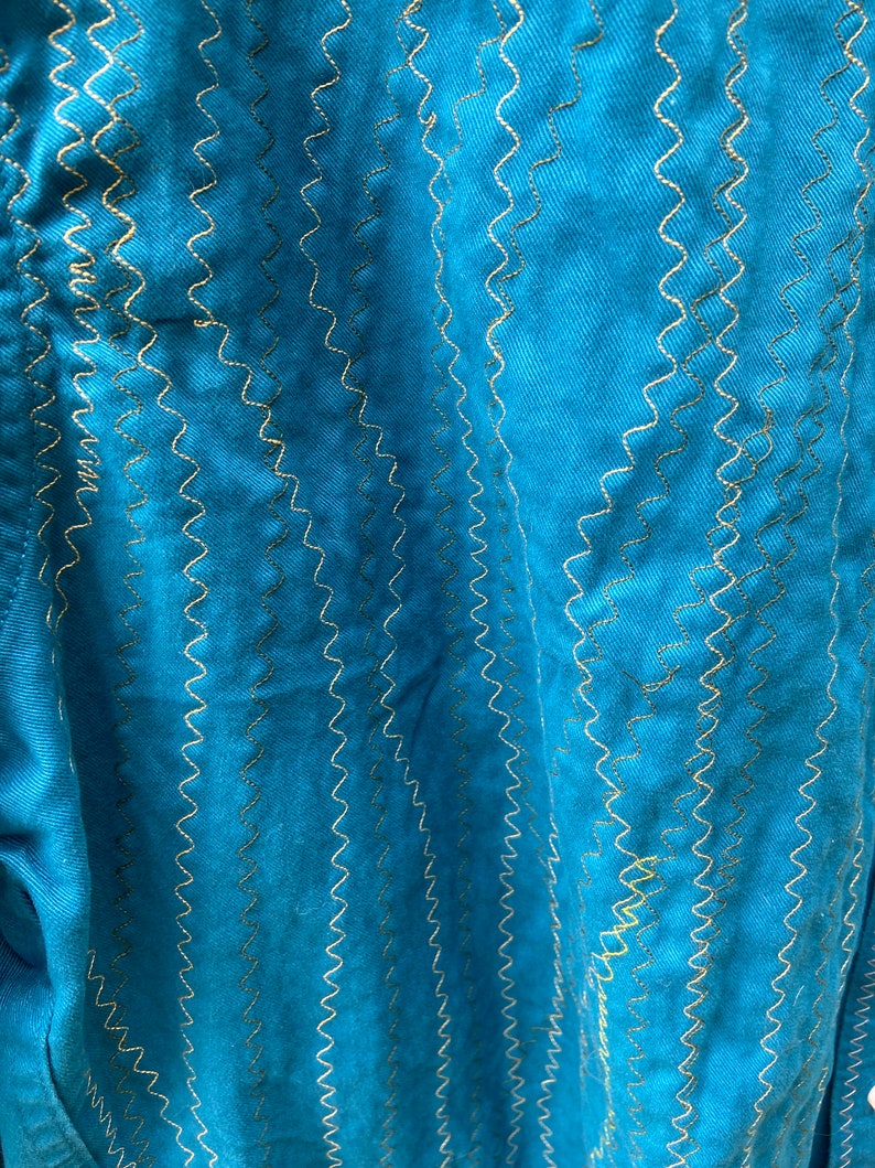 Puede incluir: Tela azul turquesa con un patr&oacute;n de costura en zigzag decorativo en hilo dorado.