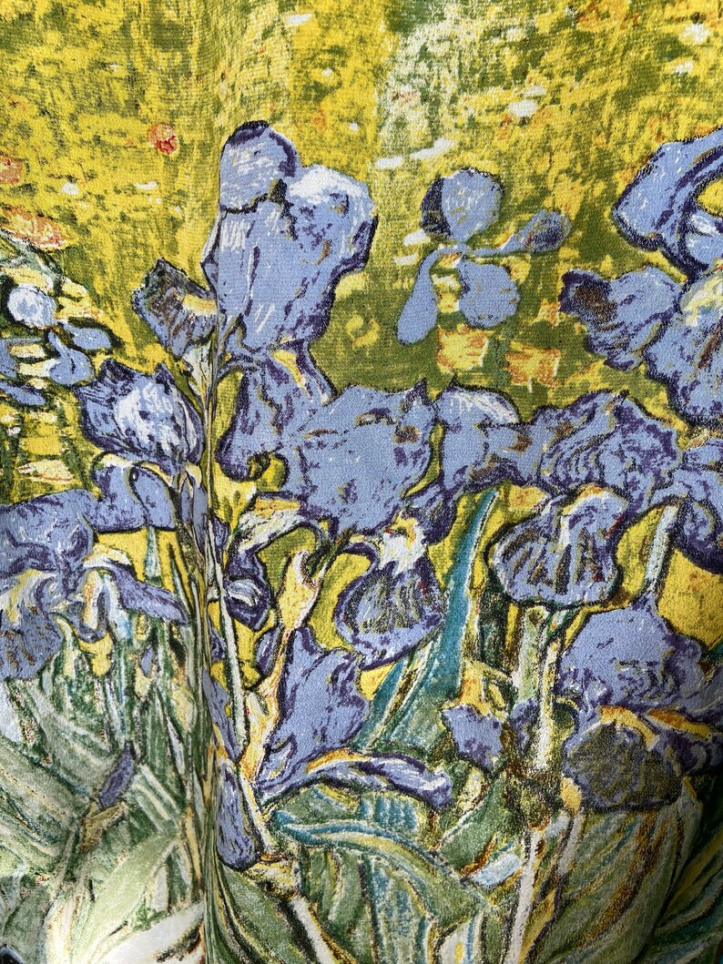 Puede incluir: Un primer plano de un tapiz con un dise&ntilde;o floral vibrante. El tapiz representa un grupo de iris p&uacute;rpuras con hojas verdes sobre un fondo amarillo. La tela tiene una apariencia texturizada y tejida.