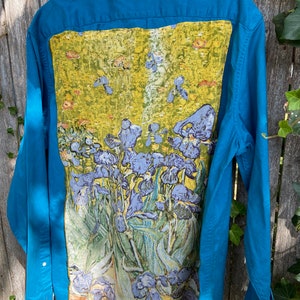 Puede incluir: Una camisa de manga larga azul turquesa con botones con una pintura de iris morados en la espalda. La pintura est&aacute; sobre un fondo amarillo con hojas verdes.