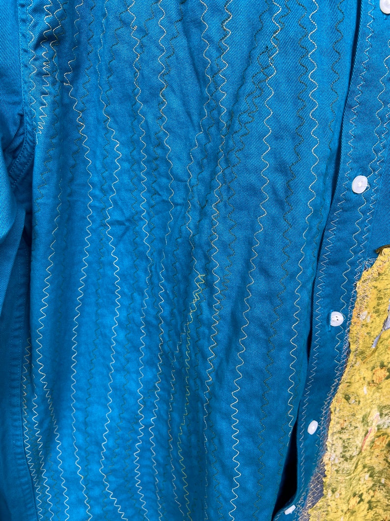 Puede incluir: Una camisa azul turquesa con un patr&oacute;n de puntadas en zigzag decorativo. La camisa tiene un frente abotonado y mangas largas.