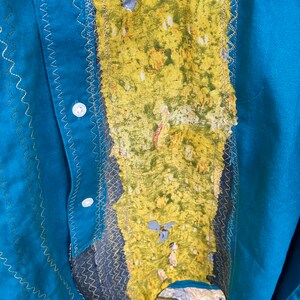 Puede incluir: Una camisa azul turquesa con una tela estampada en amarillo y verde cosida en la parte delantera. La tela est&aacute; cosida con una puntada en zigzag.