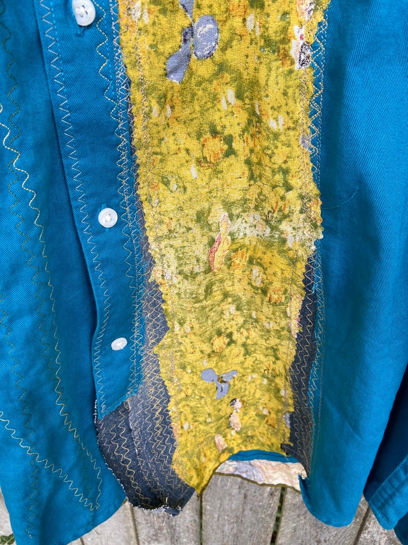 Puede incluir: Una camisa azul turquesa con una tela estampada en amarillo y verde cosida en la parte delantera. La tela est&aacute; cosida con una puntada en zigzag.