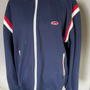 May include: A navy blue zip-up jacket with white and red stripes on the sleeves and a small red logo on the chest.