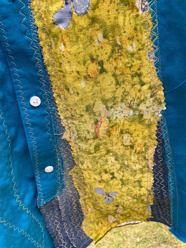 Puede incluir: Una camisa azul turquesa con un tejido estampado floral amarillo y verde cosido en la parte delantera. El tejido est&aacute; cosido con una puntada en zigzag dorada.
