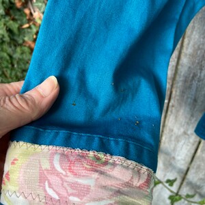Puede incluir: Una camisa de algod&oacute;n azul turquesa con un pu&ntilde;o de estampado floral. El pu&ntilde;o est&aacute; hecho de una tela rosa claro y blanca con un patr&oacute;n floral.