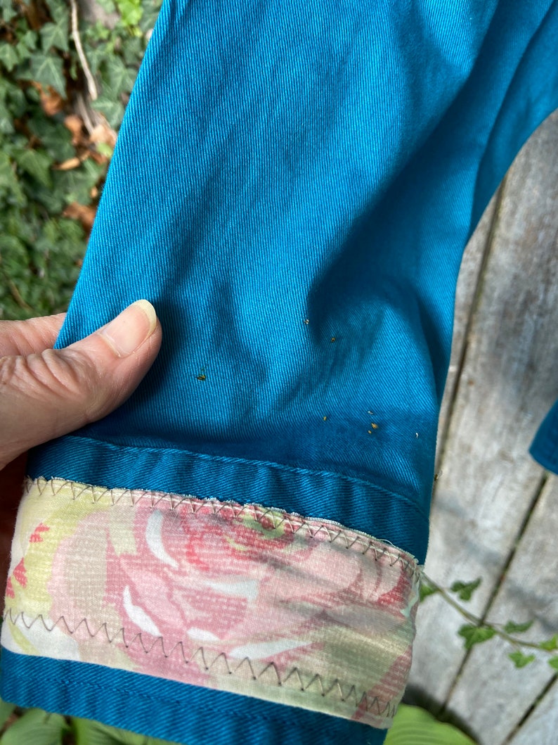 Puede incluir: Una camisa de algod&oacute;n azul turquesa con un pu&ntilde;o de estampado floral. El pu&ntilde;o est&aacute; hecho de una tela rosa claro y blanca con un patr&oacute;n floral.