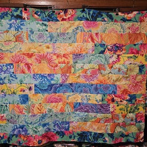May include: A colorful patchwork quilt with a variety of floral patterns in shades of blue, green, yellow, orange, and pink. The quilt is made up of many different fabric scraps sewn together in a horizontal pattern.