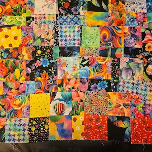 May include: A patchwork quilt in progress, featuring a vibrant array of fabric squares. Each square showcases a unique floral, butterfly, or abstract design in a kaleidoscope of colors, including red, yellow, blue, and green. The quilt is unfinished, with raw edges visible.