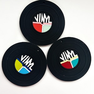May include: Three black vinyl record-shaped coasters with colorful center circles that say "VINYL" in white letters.