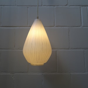 May include: A white teardrop-shaped pendant light fixture with a wood grain pattern hangs from a white brick wall.
