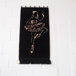 Könnte beinhalten: Eine schwarze Wandteppich mit Fransenrand zeigt eine Silhouette einer Ballerina in einem rosa Tutu, mit erhobenen Armen und einem ausgestreckten Bein.