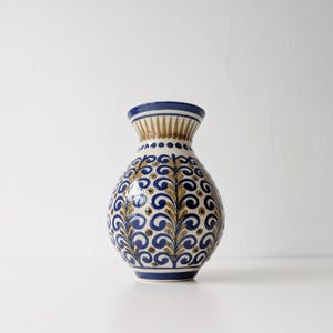 May include: A blue and gold ceramic vase with a floral pattern. The vase has a round body and a narrow neck.