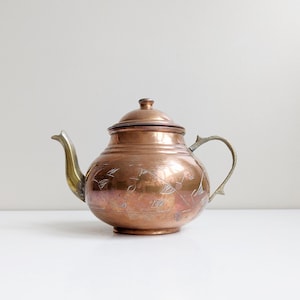 Puede incluir: Una tetera de cobre con un diseño grabado adornado y un asa y un pico de latón.