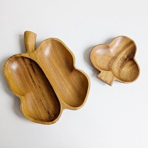 Pode incluir: Dois pratos de servir de madeira, um com a forma de um coração e o outro com a forma de uma borboleta com duas seções. Ambos os pratos são de madeira castanho claro.