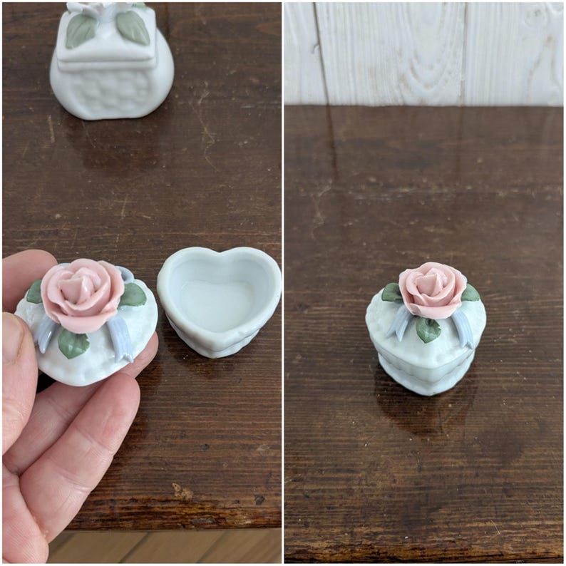 May include: Two small porcelain trinket boxes with a heart and square shape. Both boxes are decorated with a pink rose and green leaves. The boxes are white with a light blue trim.