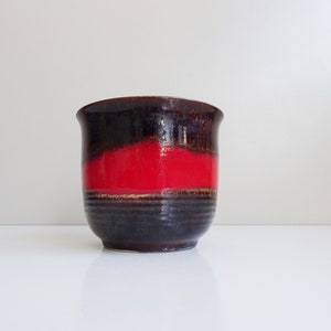 Può includere: Un vaso da fiori in ceramica marrone e rosso con un'ampia apertura e un fondo arrotondato.