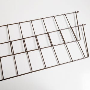 Puede incluir: Dos portarevistas de alambre metálico marrón, apilados uno encima del otro. Los portarevistas son rectangulares y tienen un patrón de rejilla.