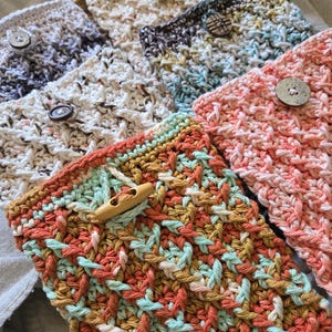 May include: A set of six crocheted phone pouches in various colors and patterns, each with a wooden button closure. The pouches are made with a variety of yarns, including white, gray, blue, pink, and orange.