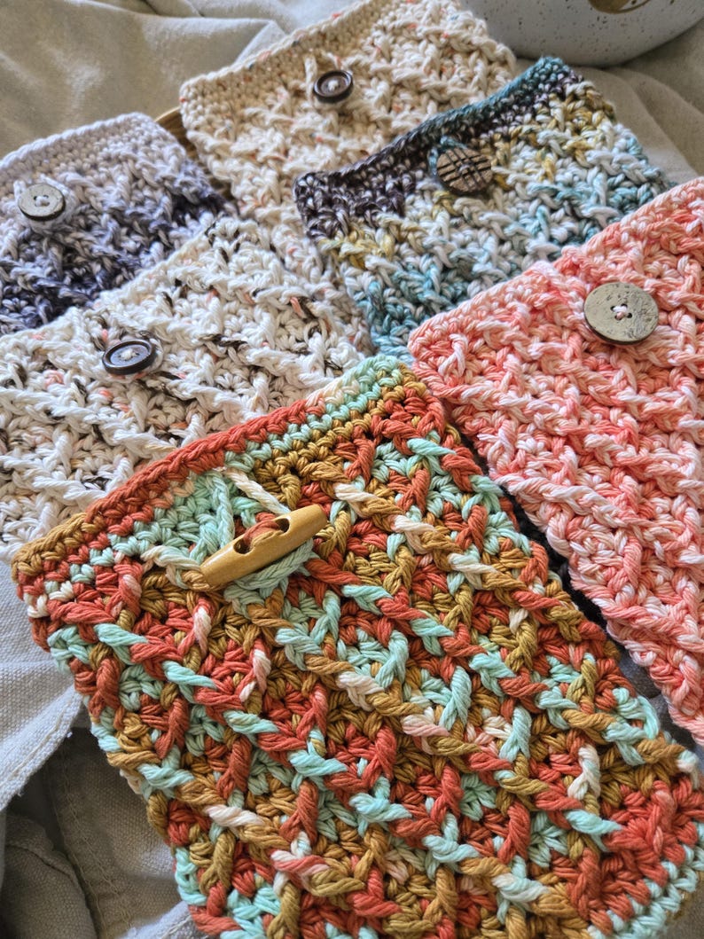 May include: A set of six crocheted phone pouches in various colors and patterns, each with a wooden button closure. The pouches are made with a variety of yarns, including white, gray, blue, pink, and orange.