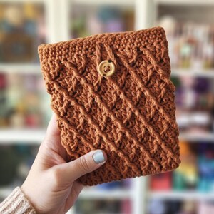 May include: A crocheted brown pouch with a wooden button closure. The pouch has a textured, woven pattern.