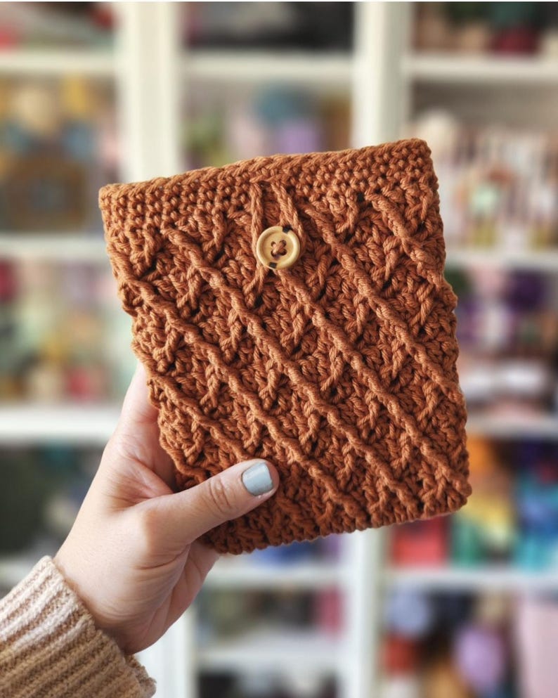 May include: A crocheted brown pouch with a wooden button closure. The pouch has a textured, woven pattern.
