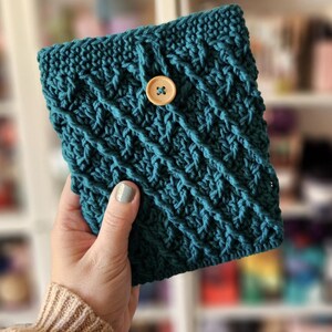 May include: A teal blue crocheted pouch with a wooden button closure. The pouch is made with a textured stitch pattern.