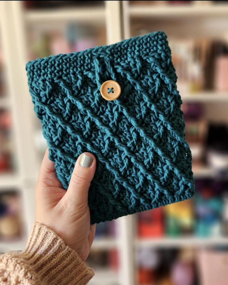 May include: A teal blue crocheted pouch with a wooden button closure. The pouch is made with a textured stitch pattern.