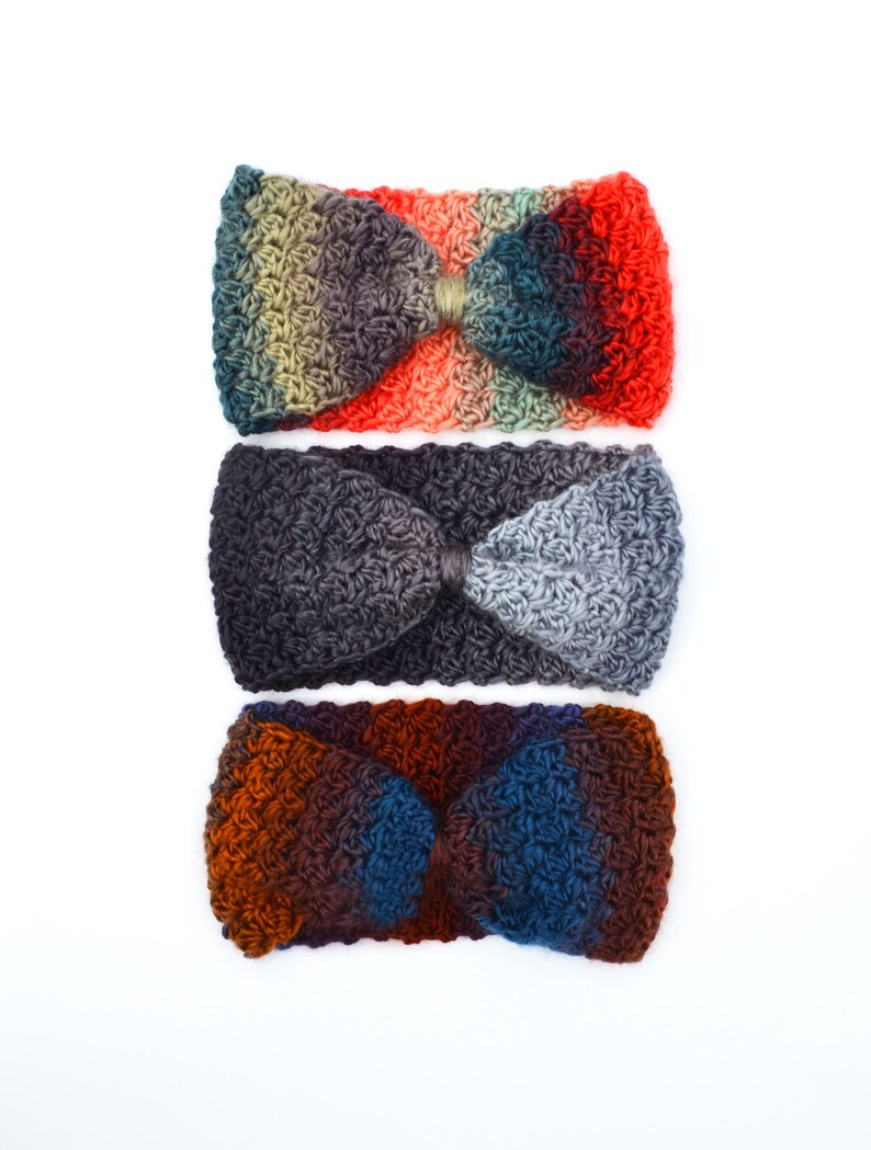 May include: Three crocheted headbands in a row, each with a bow-like design. The top headband transitions from green to red, the middle one is gray, and the bottom one shifts from brown to blue. All are set against a white background.