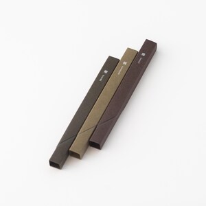 May include: Three brown, green, and dark brown incense sticks in their packaging. The packaging is made of paper and has Japanese characters printed on it. The sticks are arranged in a row, with the brown stick on top, the green stick in the middle, and the dark brown stick on the bottom.