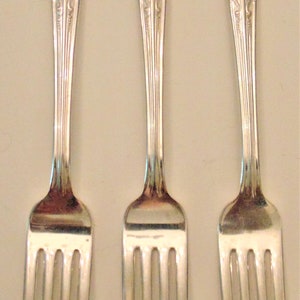 May include: Three silver forks with ornate handles and five tines each.