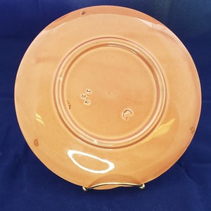 Może przedstawiać: Sp&oacute;d talerza ceramicznego w kolorze brzoskwiniowym z podniesionym rantem. Talerz ma znak producenta z napisem "Made in England" i mały okrągły znak.