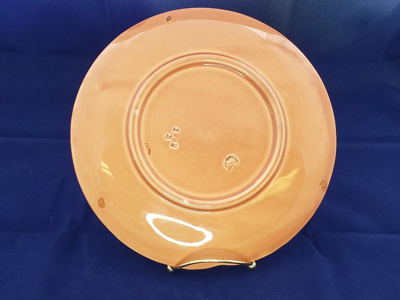 Może przedstawiać: Sp&oacute;d talerza ceramicznego w kolorze brzoskwiniowym z podniesionym rantem. Talerz ma znak producenta z napisem "Made in England" i mały okrągły znak.