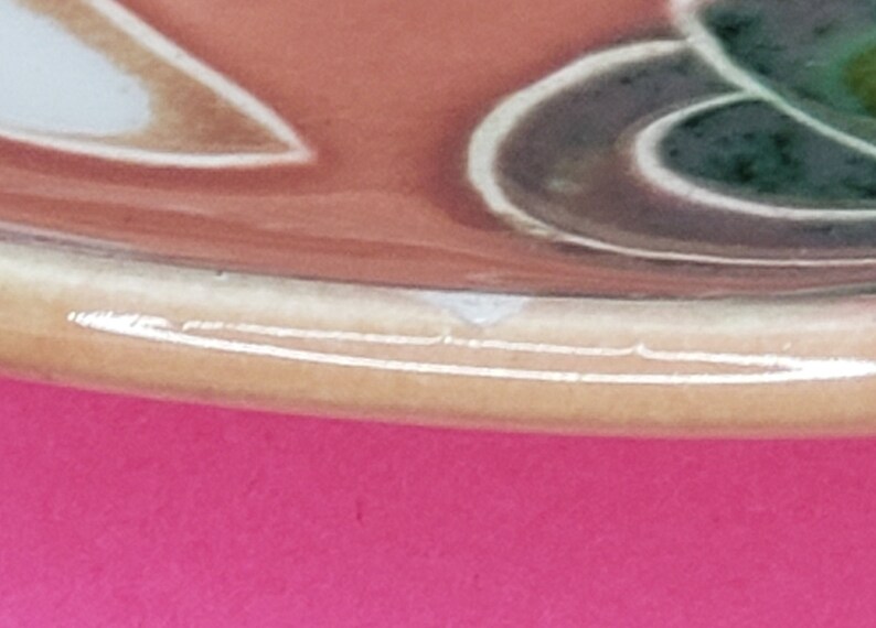 Może przedstawiać: Zbliżenie na dolną krawędź ceramicznej miski z brązową, pomarańczową, zieloną i białą glazurą. Miska ma lekko zaokrąglony brzeg.